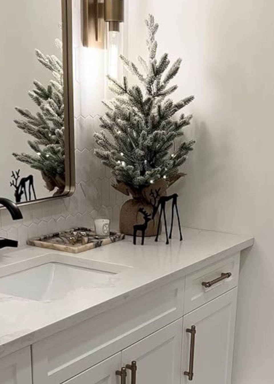 Flocked Christmas tree with small black deer figurines on a bathroom counter