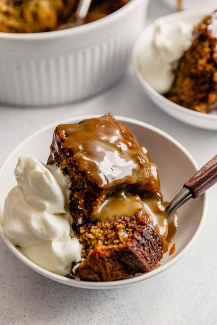 A bowl of sticky toffee pudding drizzled with caramel sauce and whipped cream