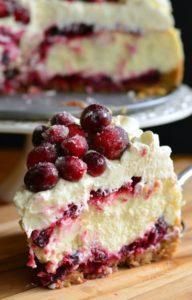 A slice of cranberry cheesecake topped with sugared cranberries on a graham crust