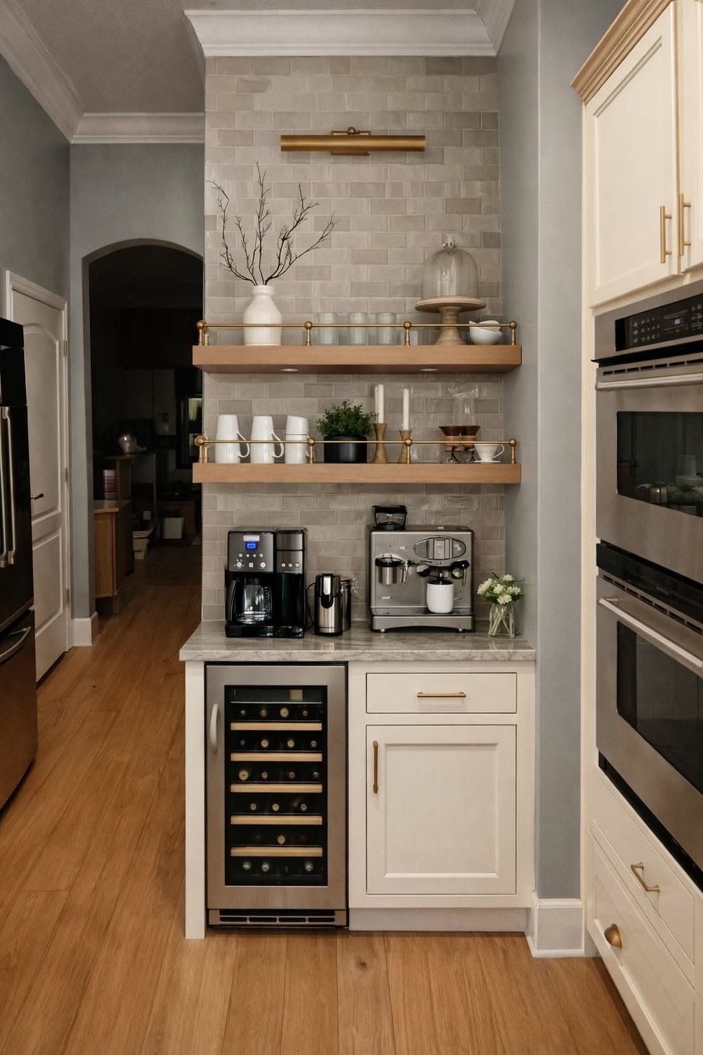 Beige tile backsplash behind brass-railed shelves, a picture light and coffee machines above a wine fridge and cream cabinet