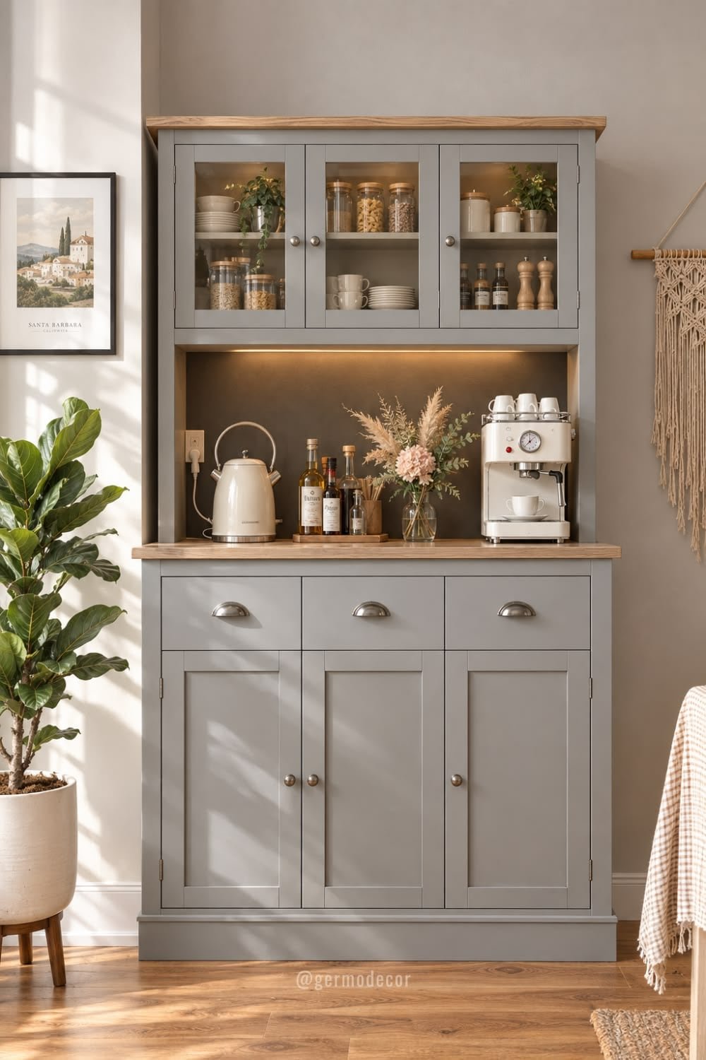 Gray kitchen hutch with glass-front cabinets, a wood top, a kettle, espresso machine and dried flowers, beside a fiddle-leaf fig