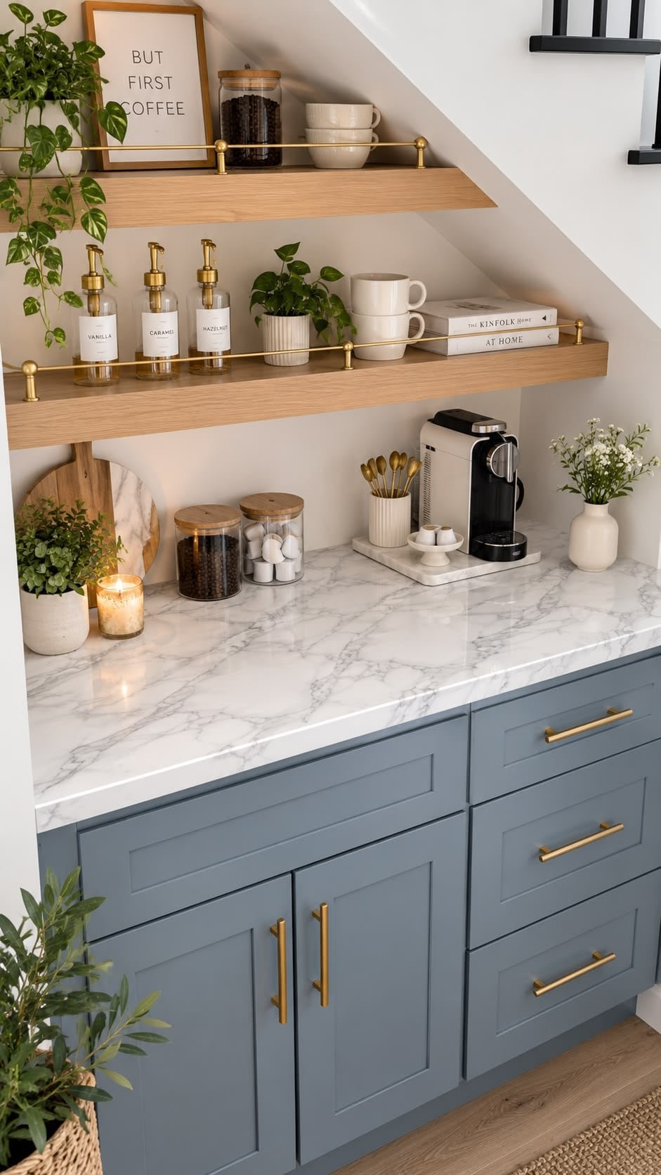 Marble-look counter with a coffee maker, glass jars, mugs, a small plant and a candle beneath brass-railed floating shelves
