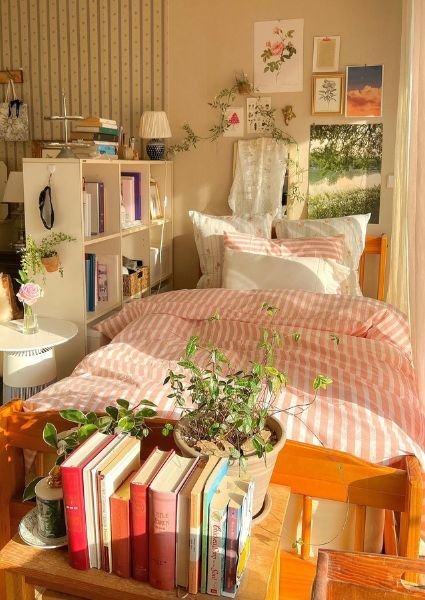 Pink striped bedding with a stack of books in a pastel cottagecore bedroom