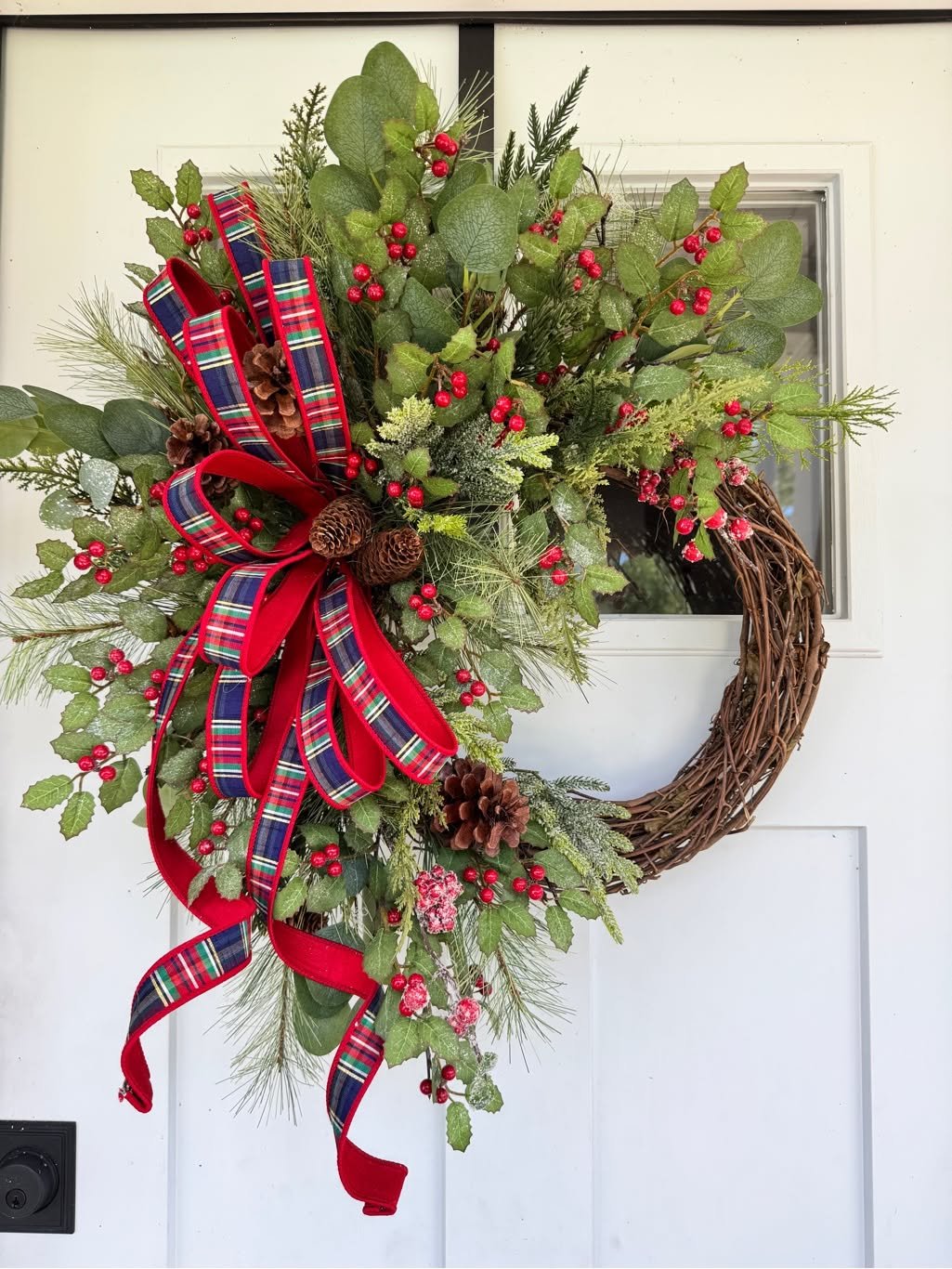 Eucalyptus and berry wreath with a red and navy plaid bow on a white door