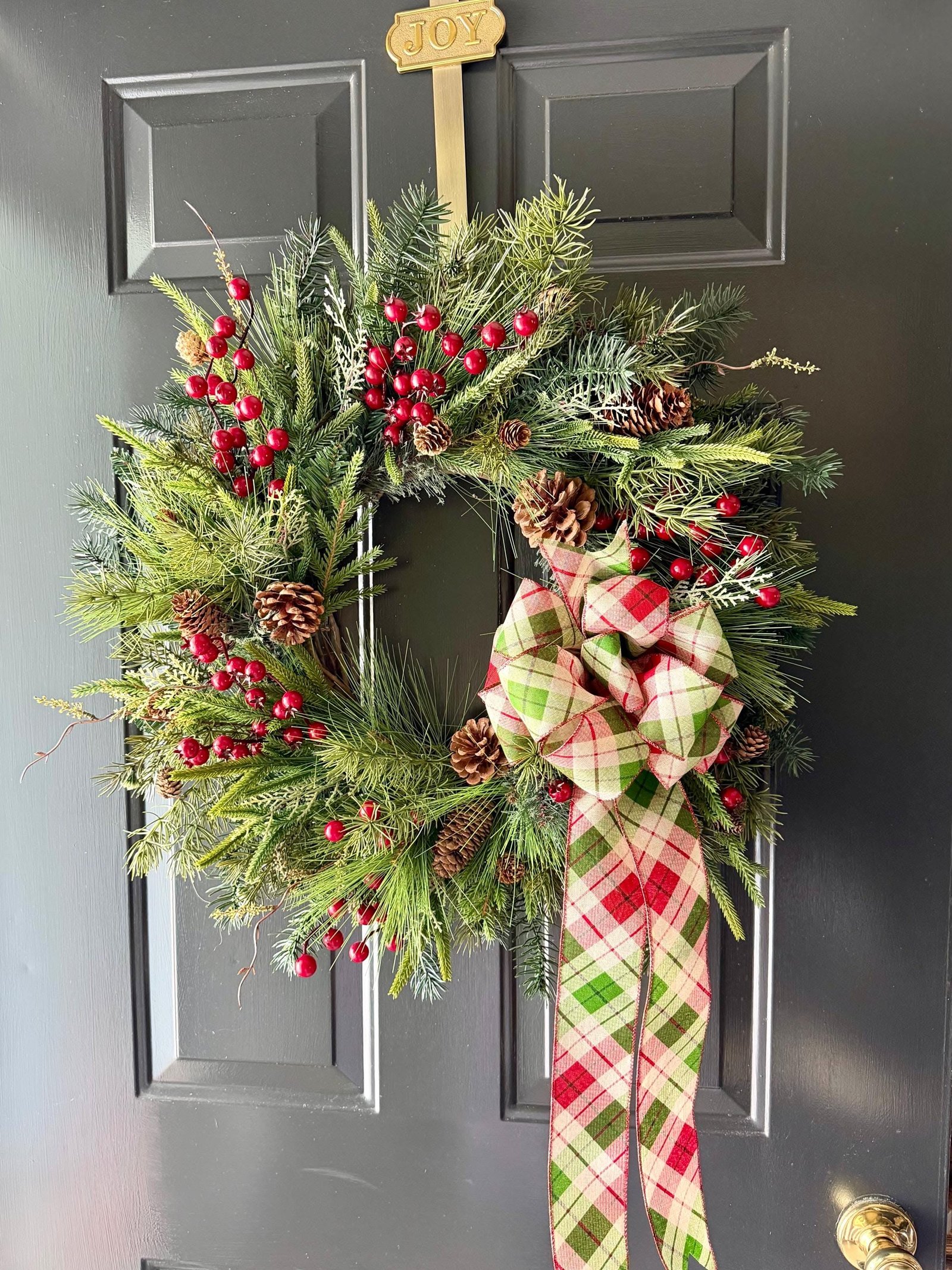 Pine and berry wreath on a dark door with a small Joy sign above