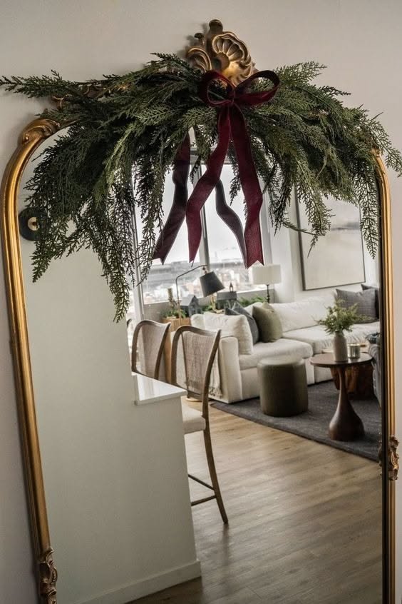 Arched mirror decorated with greenery garland and a burgundy ribbon bow
