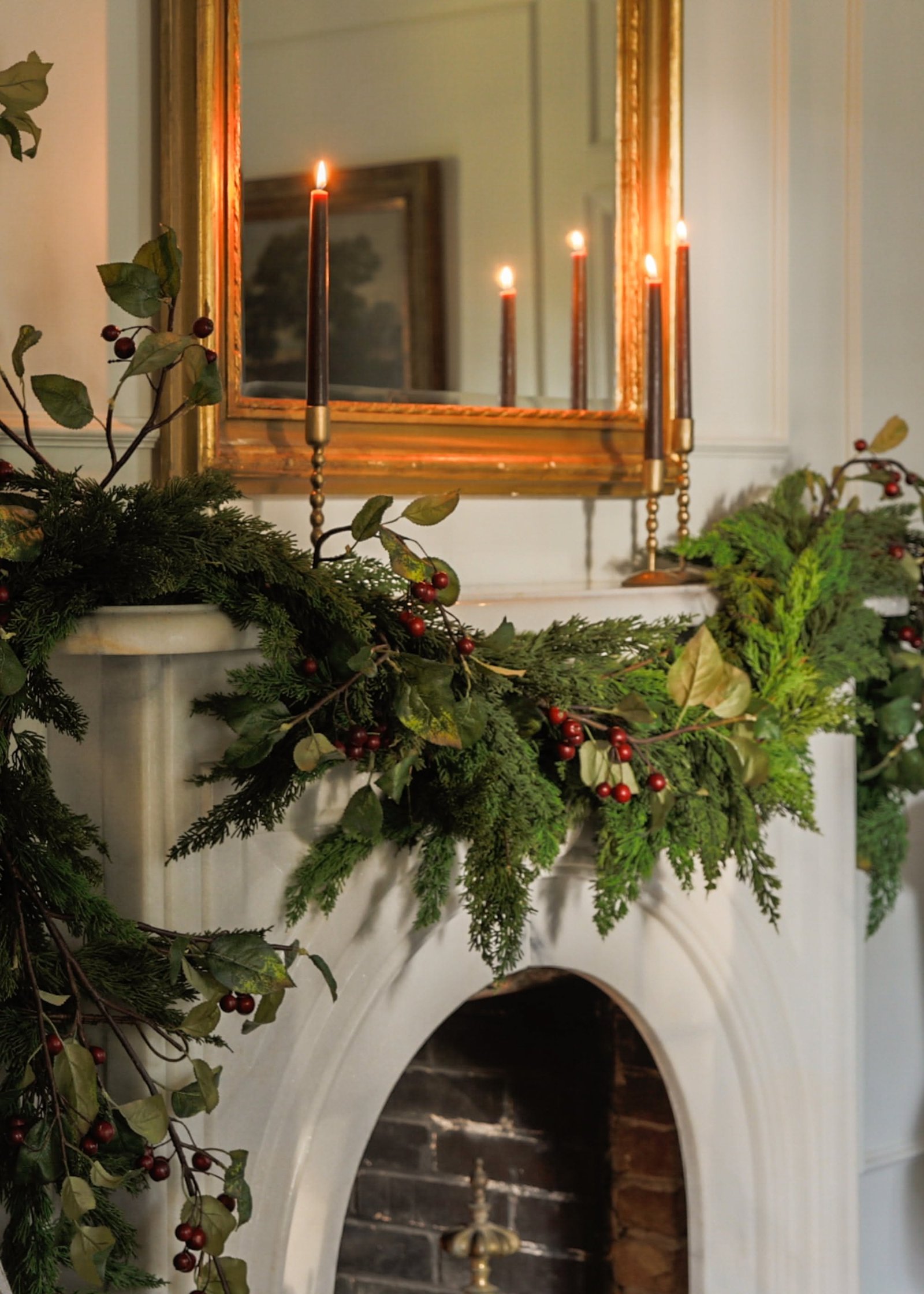 Fireplace mantel with antique brass candlesticks, candles, and fresh greenery garland