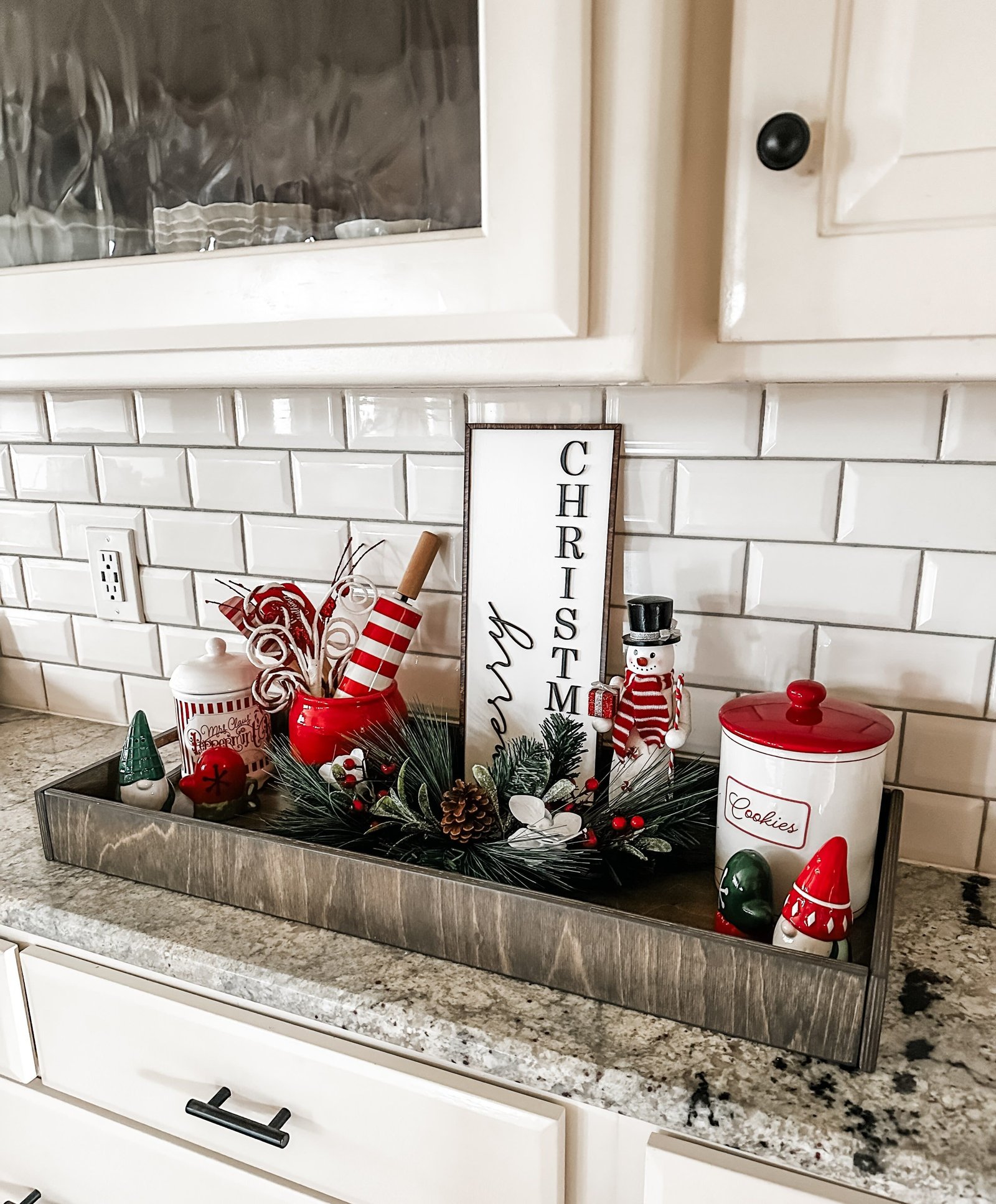 A wooden tray with gnomes, a snowman jar, and a vertical Merry Christmas sign