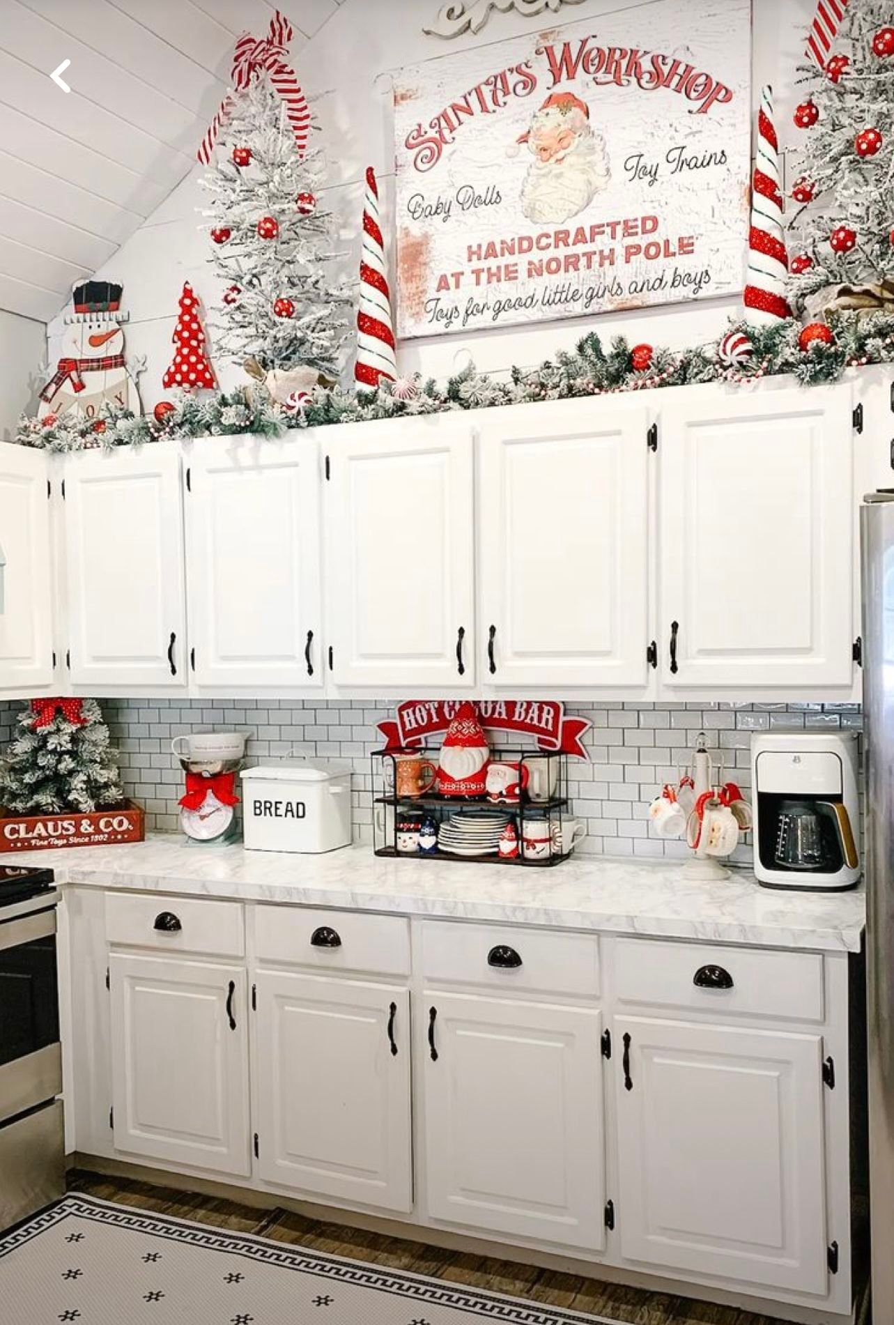 A Santas Workshop sign mounted above white kitchen cabinets with flocked trees