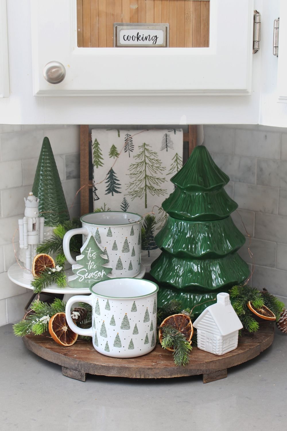 A green ceramic Christmas tree canister with mugs on a kitchen counter