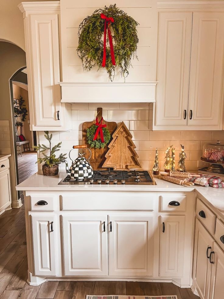 A greenery wreath hanging from a wood tree cutting board on a stove backsplash
