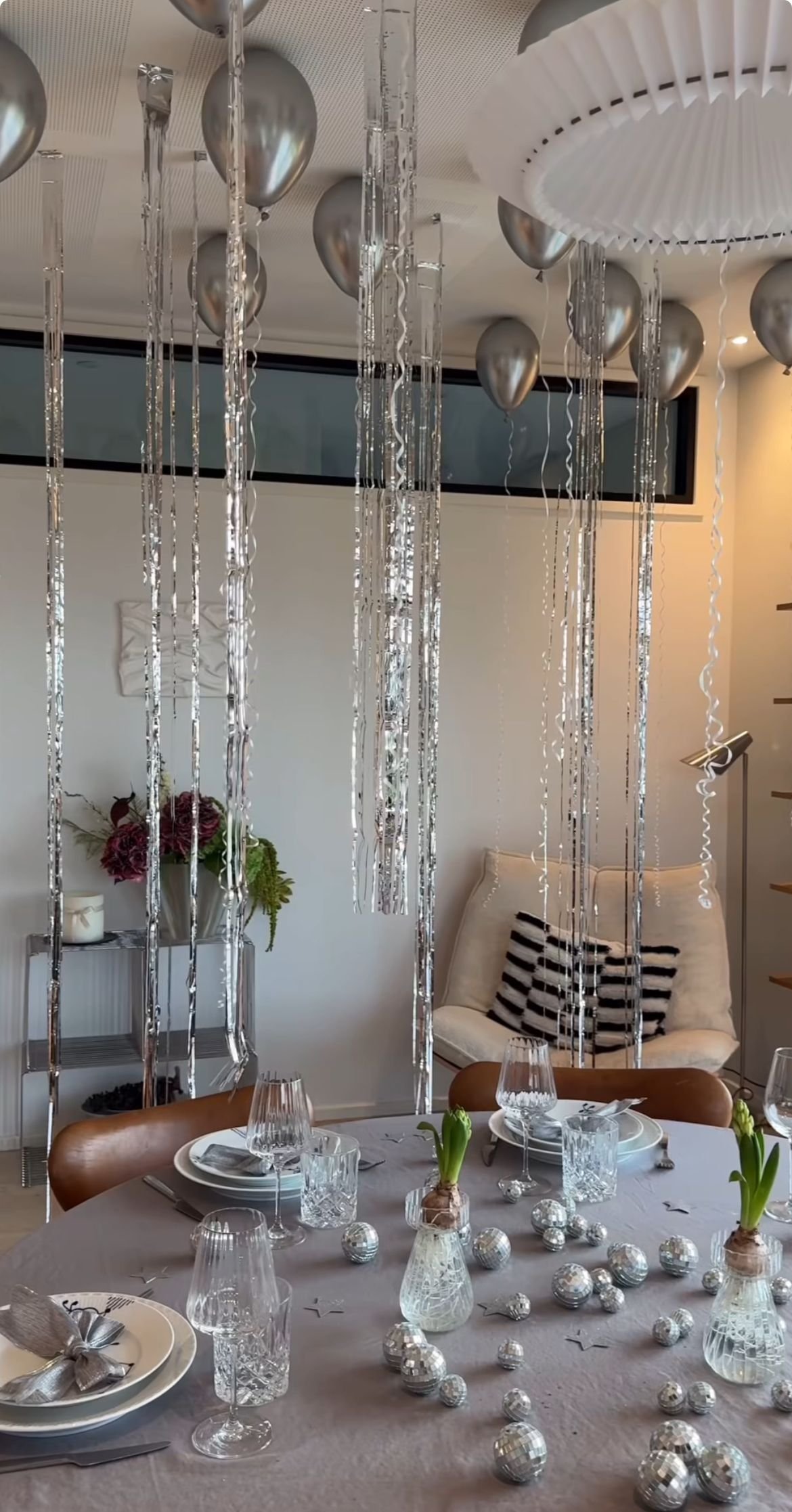 Silver mirrored tinsel streamers and balloons hanging over a dinner table with place settings