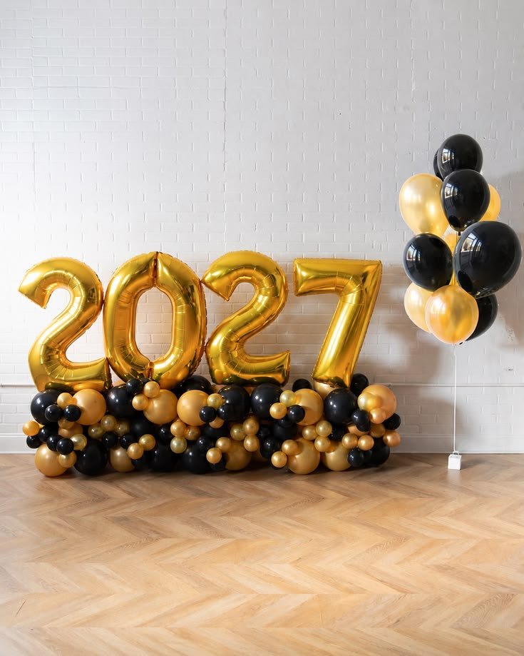 Large gold 2027 balloon numbers on a wood floor with a black and gold balloon cluster