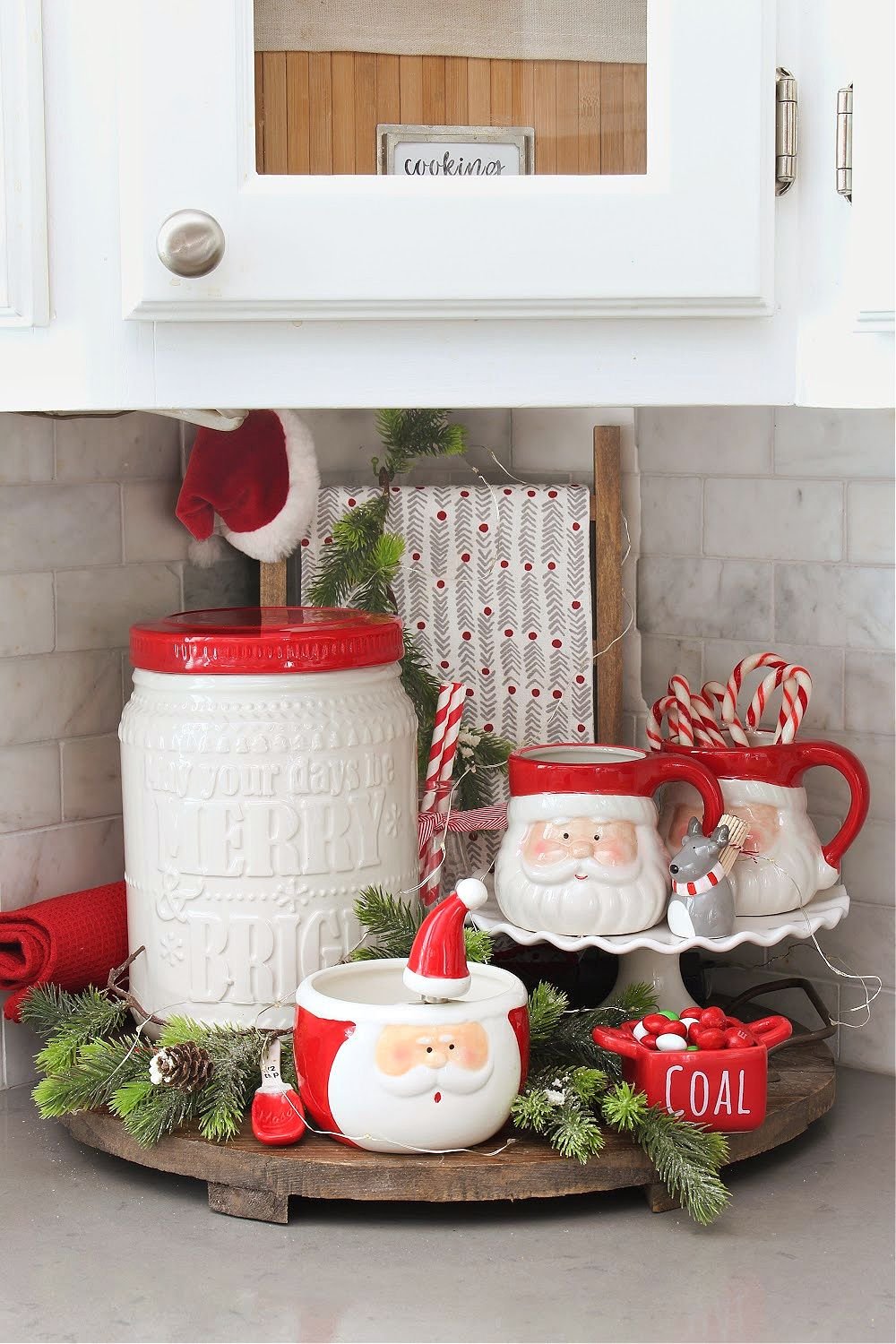 Wooden tray styled as a hot cocoa bar with Santa mugs, candy canes, and a Coal dish