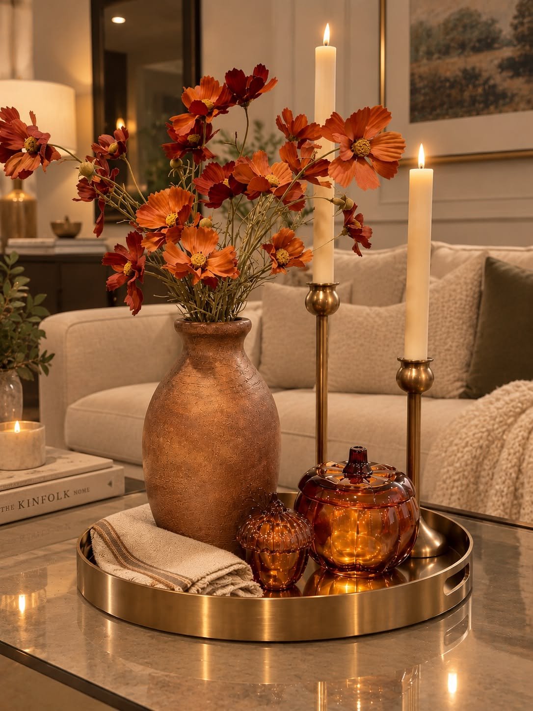 Tray with amber glass candles and a copper vase of orange flowers